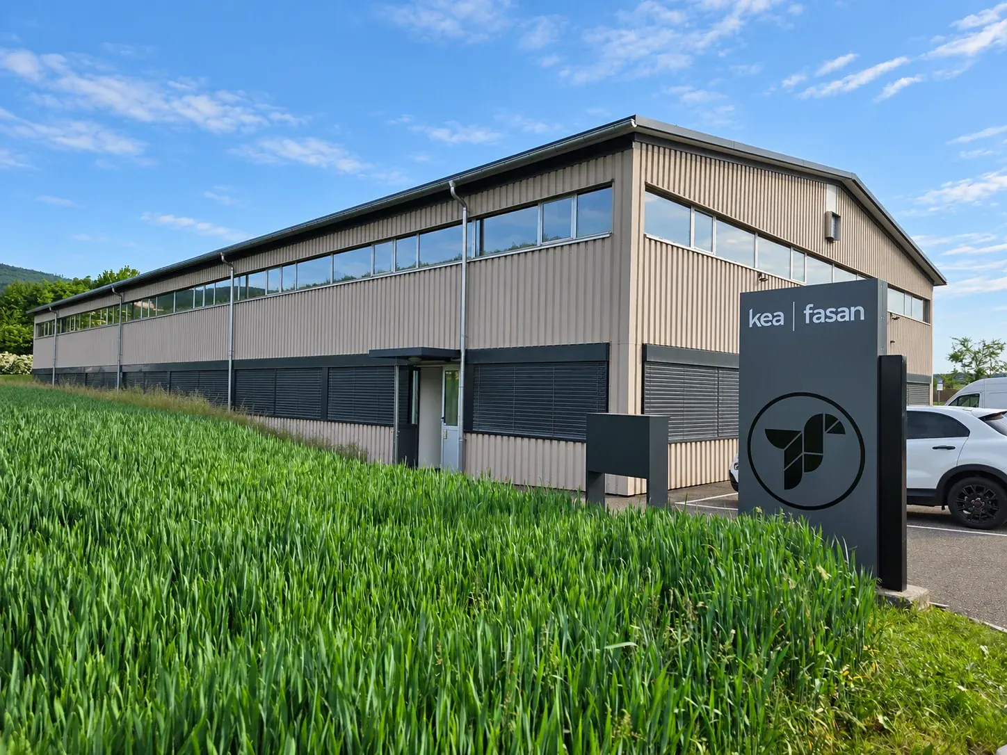 KEA-Hauptgebäude mit kea | fasan-Schild vor dem Eingang und Getreidefeld im Vordergrund